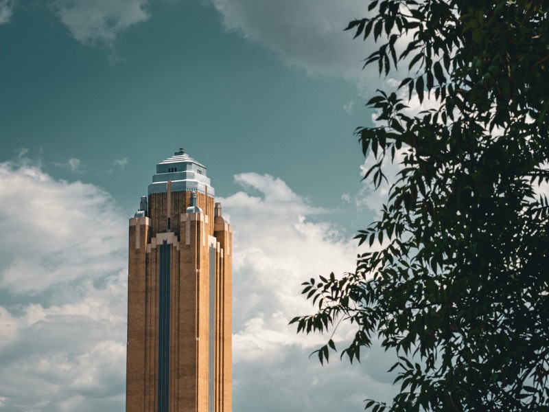 An Art Deco tower framed by trees beneath a cloudy sky.